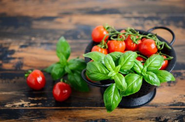 Fresh red cherry tomatoes with basil on a wooden background.