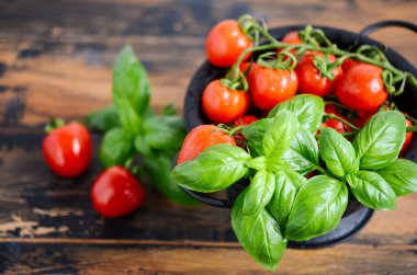 Fresh red cherry tomatoes with basil on a wooden background.