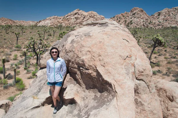 A chinese woman standing on large boulders within the desert ecosystem in Joshua Tree National Park in sunny california.