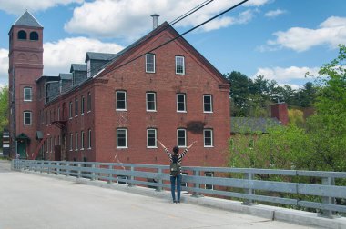 Yarmouth Maine 'de güneşli mavi bir günde Royal River' da bulunan tarihi Sparkhawk değirmeninin dışında kutlama yapan bir kadın..