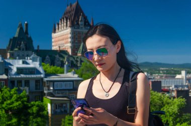 Eski Quebec şehrinde güneşli bir günde cep telefonuna bakan Çinli bir kadın..