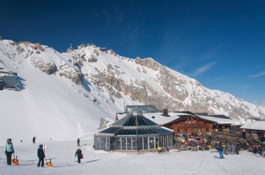 Garmisch-Partenkirchen, Almanya. 6 Mart. 2022 yılı. Zugspitze 'deki kayak yamaçlarındaki binalar ve insanlar ve Garmisch-Partenkirchen Almanya' daki Wetterstein dağları bir kış günü.