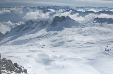 Karla kaplı Wetterstein dağlarının panoramik manzarası ve Garmisch-Partenkirchen Almanya 'sındaki zugspitze tepesinden bulutlarla kaplı kayak yamaçları.