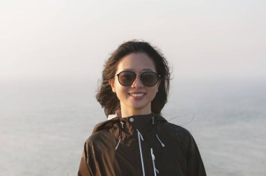 a happy asian woman smiling with a foggy ocean background in the afternoon sun on martha's vineyard. clipart