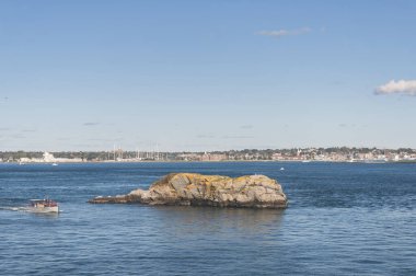 Jamestown Rhode Island 'daki Fort Wetherill eyalet parkında büyük bir kayanın yanından geçen küçük bir tekne.