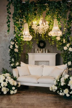 Beyaz kanepe, beyaz çiçekler, merdivenler, şömine, avizeler ve mumlarla dolu fotoğraf stüdyosu.