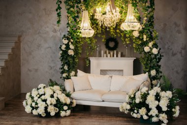 Beyaz kanepe, beyaz çiçekler, merdivenler, şömine, avizeler ve mumlarla dolu fotoğraf stüdyosu.