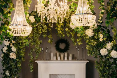 Beyaz kanepe, beyaz çiçekler, merdivenler, şömine, avizeler ve mumlarla dolu fotoğraf stüdyosu.