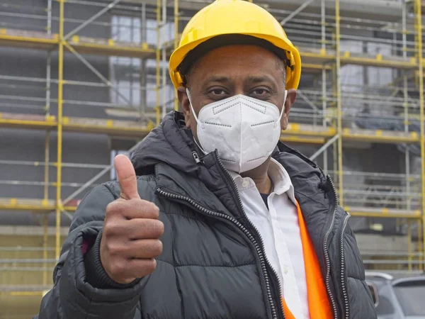 Indian construction worker wearing a protective ffp2 mask posing on construction site showing thumbs up gesture