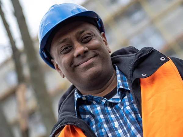 Portrait of a smiling Indian civil engineer or factory worker wearing a blue safety helmet and looking at camera