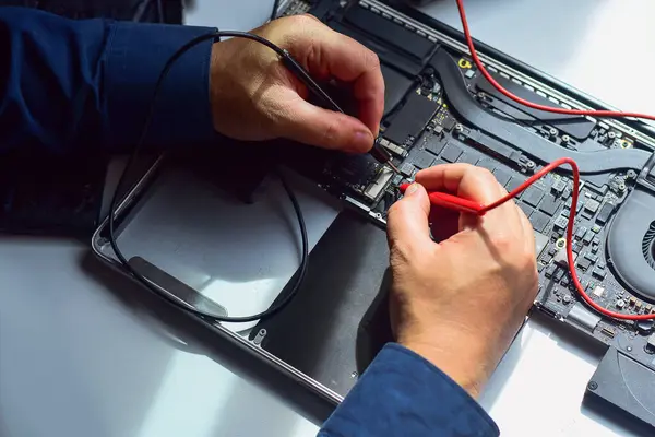 Bilgisayar teknisyeni bir dizüstü bilgisayar anakart tamircisi masasındaki arızaları bulmak için IC sayacını kullanıyor. Modern teknolojiyi kullanarak tahta onarımı