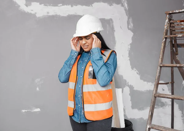 A young South Asian construction worker rubs her temples in pain on site High quality photo