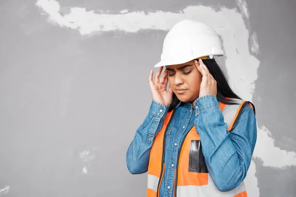 A young South Asian construction worker rubs her temples in pain on site High quality photo