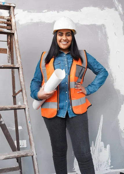 An attractive South Asian construction worker holds building plans under her arm. High quality photo