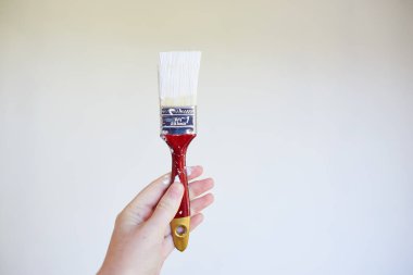 Close up of hand holding paintbrush with white paint against painted wall. High quality photo
