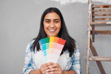 A young Indian woman holds up bright paint swatches to paint repaired wall. High quality photo