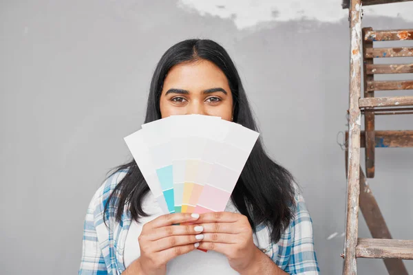 A young Indian woman holds up pale paint swatches to paint repaired wall. High quality photo