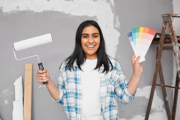 Young Indian woman poses with paint, brush, swatches getting ready to paint wall. High quality photo