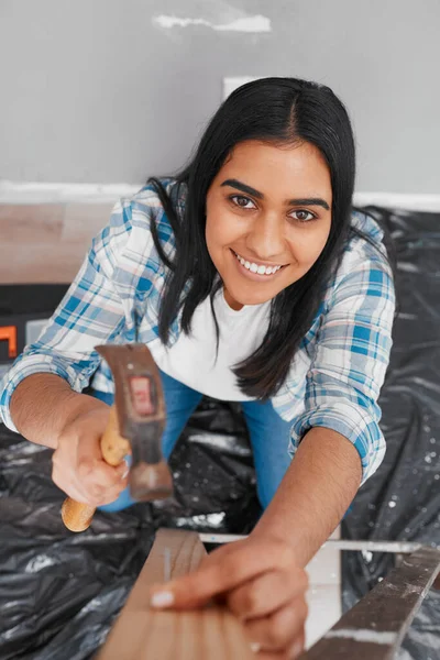 An attractive young Indian woman hammers a nail into wood home DIY. High quality photo