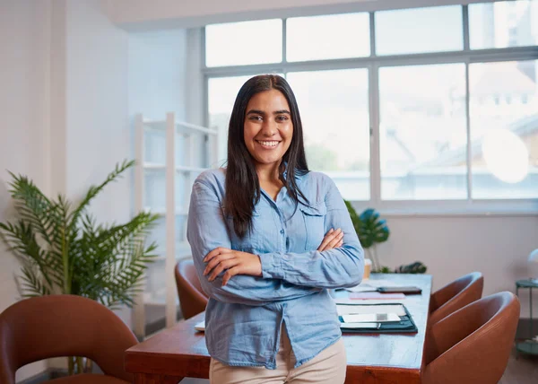 Young Indian woman stands in office arms folded, modern boardroom plants. High quality photo