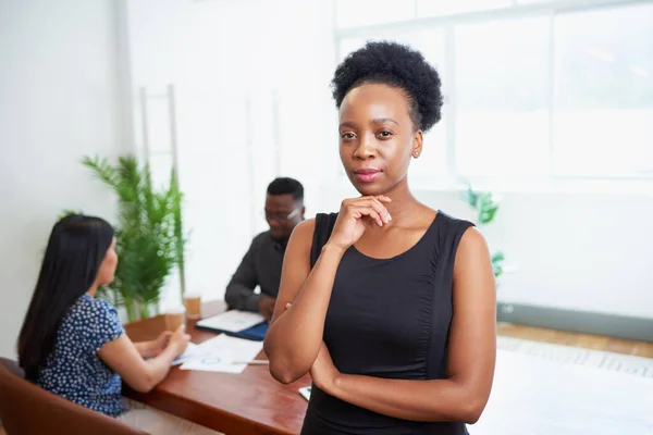 Portrait of serious young Black business woman hand to chin in boardroom. High quality photo