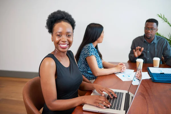 Young Black woman types on laptop at boardroom meeting with colleagues. High quality photo
