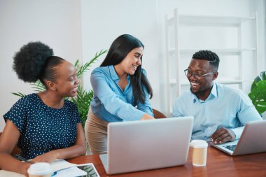 Üç gülümseyen iş arkadaşı ofiste el kol hareketi yaparken dizüstü bilgisayara bakar. Yüksek kalite fotoğraf
