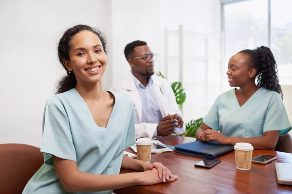 Portrait of nurse or doctor in scrubs sitting at boardroom table with colleague. High quality photo