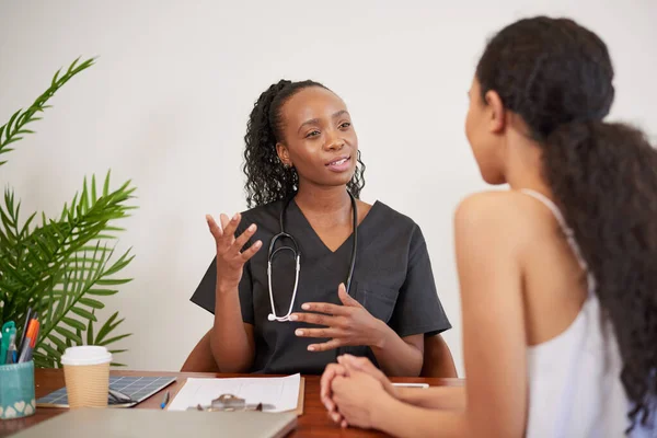 Candid shot of Black female doctor explaining to patient during GP consultation. High quality photo