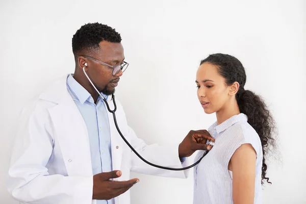 Black male doctor listens to female patients heartbeat, tells her breathe out. High quality photo