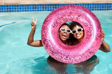 Two Black friends pose with their heads inside pink inflatable pool ring. High quality photo clipart