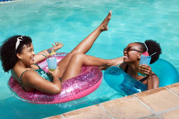 Two young friends relax in the pool, kicking leg in air laughing and drinking. High quality photo