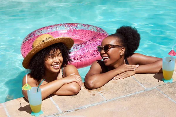 Two Black friends lean on the side of the pool, relaxing in water with mocktails. High quality photo
