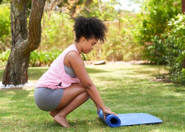 Çok ırklı genç bir kadın park bahçesindeki çimlere yoga minderini açıyor. Yüksek kalite fotoğraf