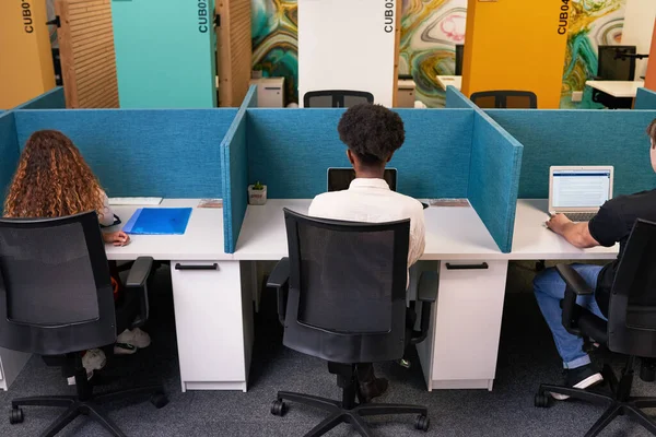 Three young people share coworking space, work side by side with desk dividers. High quality photo