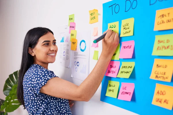 Indian woman writes ticket in backlog of colourful scrum board, KANBAN coding. High quality photo