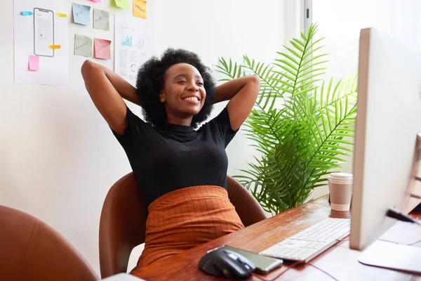 リラックスした幸せな黒の女性はオフィスの机で頭の後ろに腕で座っています 高品質の写真 — ストック写真