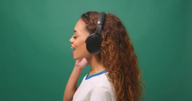 Genç, çok ırklı bir kadın kulaklıkla müzik dinliyor, dans ediyor, yeşil bir stüdyo. Yüksek kalite 4k görüntü