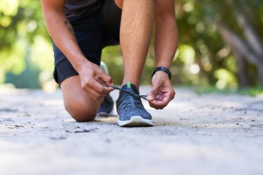 Genç bir adamın parkta koşmadan önce bağcıklarını bağlarken çekilmiş bir fotoğrafı. Yüksek kalite fotoğraf
