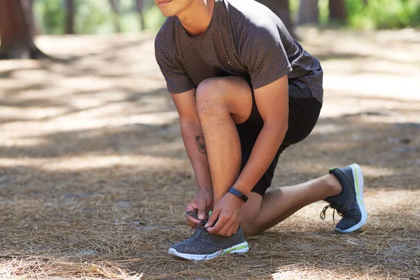 Anonymous Asian man ties shoelace in forest, ready for trail running outdoors. High quality photo