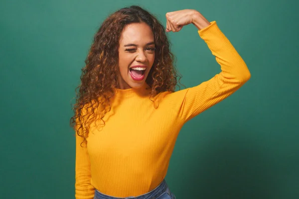 Powerful strong woman flexes arm muscle, winks smiles, greens studio background. High quality photo