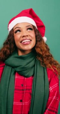 Güzel genç bir kadın Noel stüdyosunda Noel Baba şapkası takarak gülümsüyor ve yukarı bakıyor. Yüksek kalite 4k görüntü