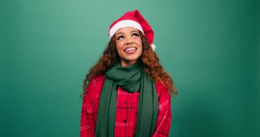 Güzel genç bir kadın Noel stüdyosunda Noel Baba şapkası takarak gülümsüyor ve yukarı bakıyor. Yüksek kalite 4k görüntü
