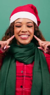 Mutlu genç kadın gülümsemeyi, Noel temalı stüdyoyu ve Noel şapkasını işaret ediyor. Yüksek kalite 4k görüntü