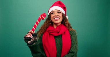 Heyecanlı genç kadın baston şeker süslemesi yapıyor, Noel şapkası stüdyosu. Yüksek kalite 4k görüntü