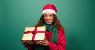 Güzel genç bir bayan Noel hediyesini elinde tutuyor, Noel Baba şapkası stüdyosunda gülümsüyor. Yüksek kalite 4k görüntü