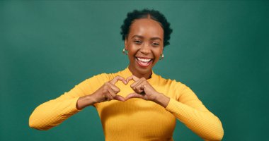 Genç siyahi kadın elleri yana, gülümseyen yeşil stüdyo ile kalp oluşturur. Yüksek kalite fotoğraf