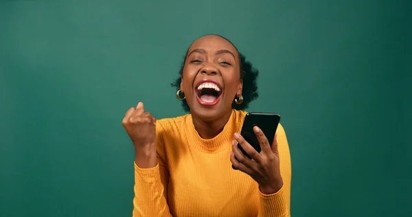 Young Black woman reads text message shocked excited, green studio background. High quality photo