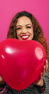 Güzel genç bir kadın kalp şeklinde balonları havaya fırlatır kahkahalar atarak, stüdyoda. Yüksek kalite 4k görüntü