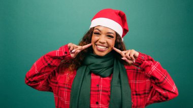 Noel stüdyosunda Noel Baba şapkası takan güzel bir genç kadın gülümsemeyi işaret ediyor. Yüksek kalite fotoğraf